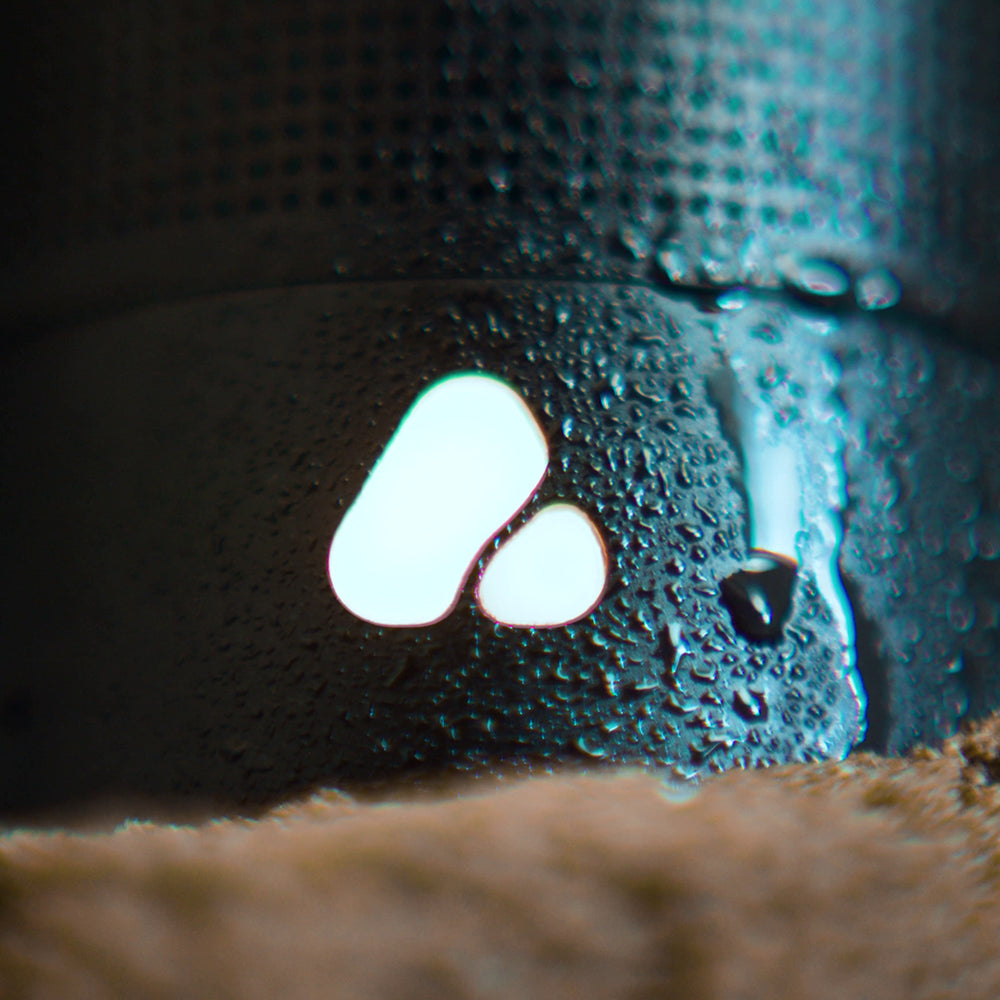 Close up of POCA audio logo on cylindrical speaker with water droplets and sand base.