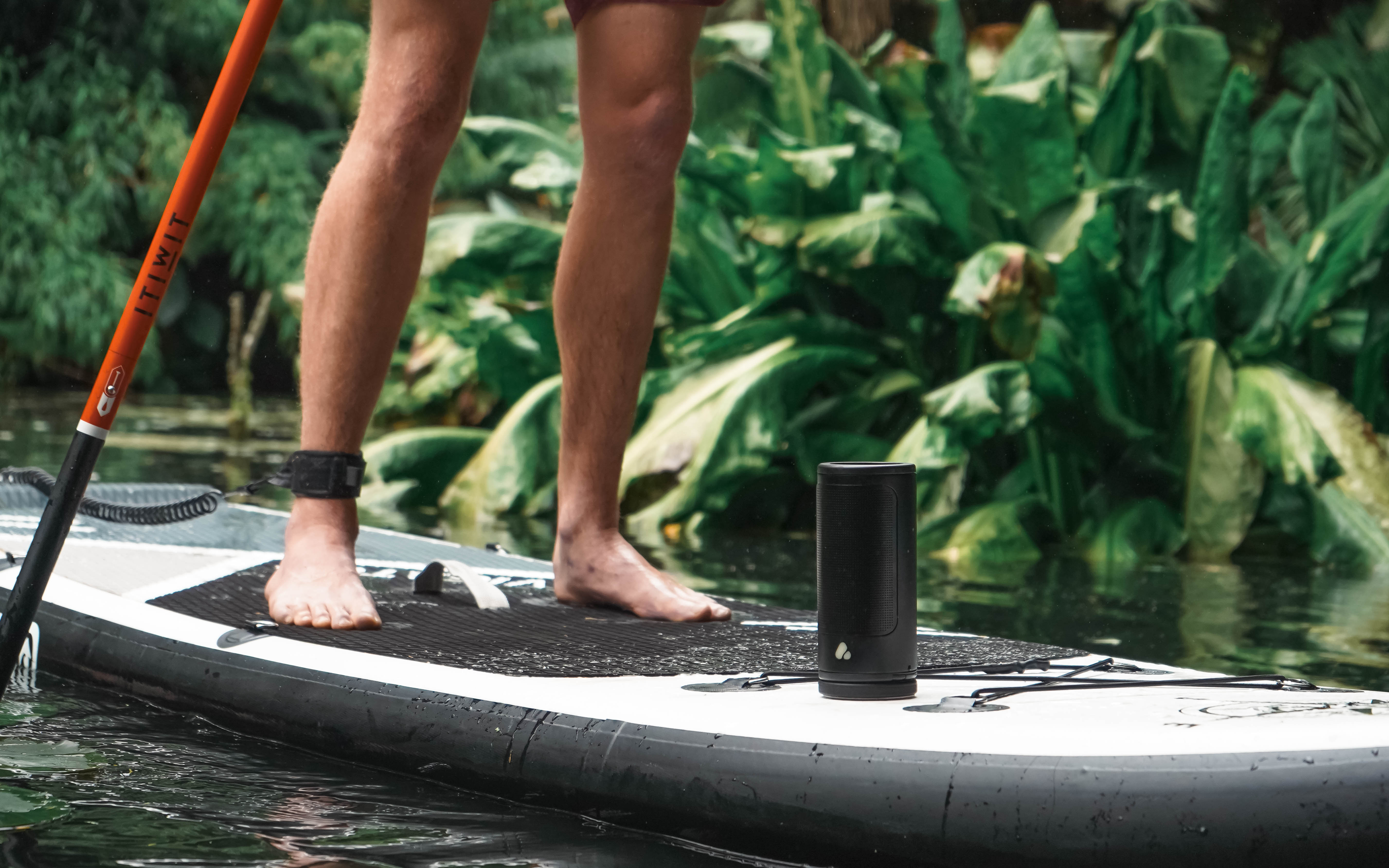 Black portable speaker attached to a paddleboard in a forest river