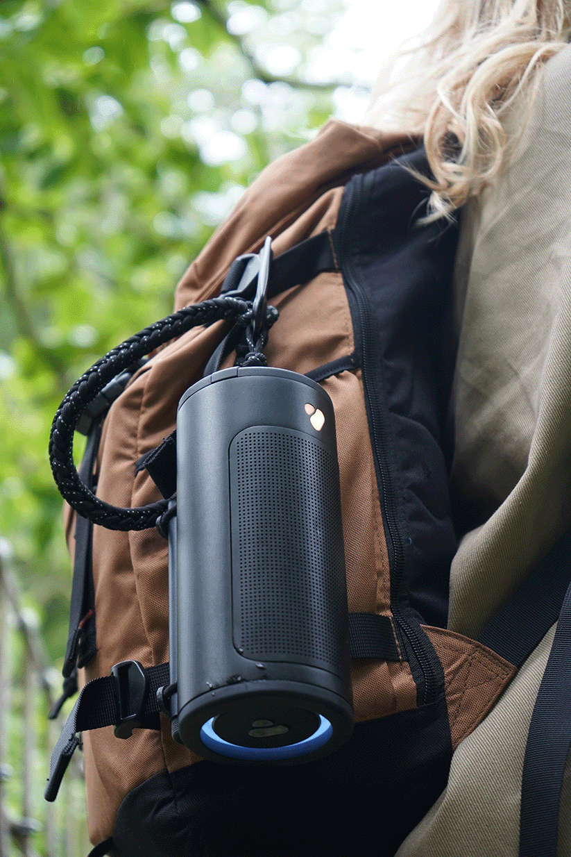 Black outdoor speaker hanging from a brown backpack.
