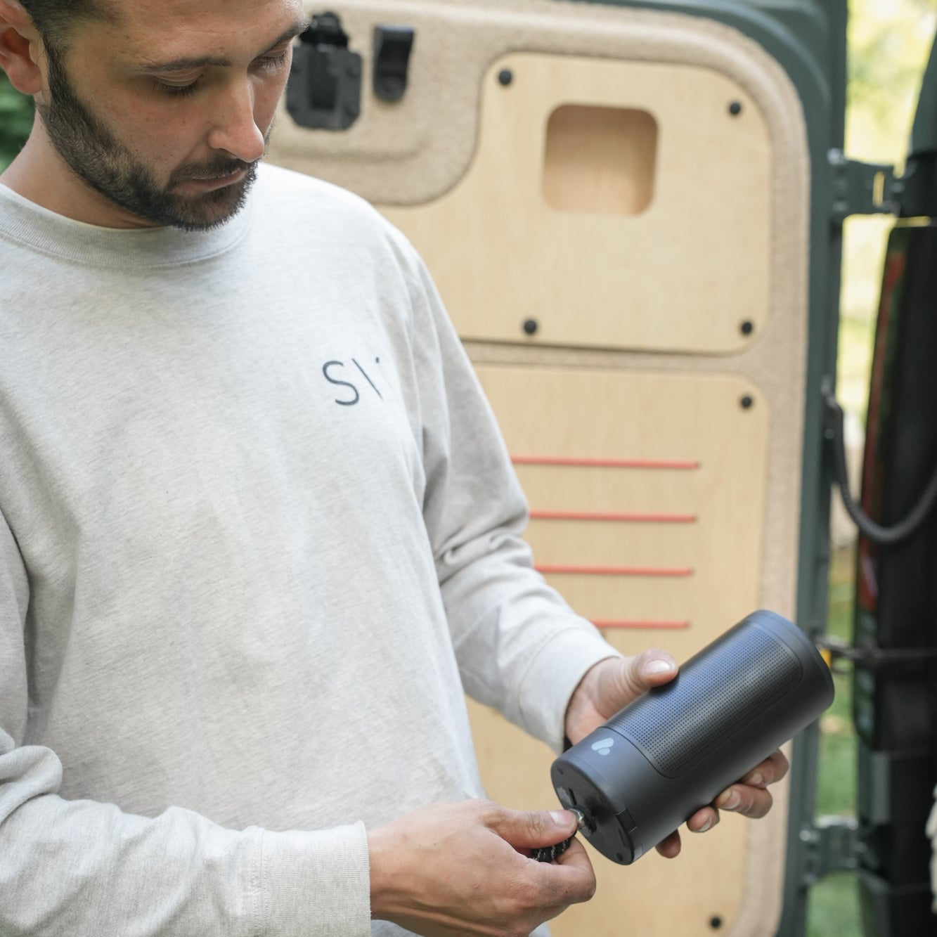 Man holding a PINE Beat bluetooth speaker near an open van door.